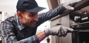 Technician in gloves inspecting a stainless steel wall oven during an oven repair in Charlotte